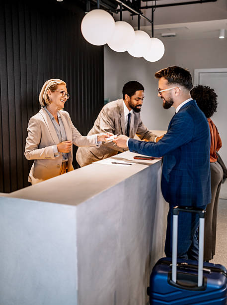 Businessman receiving a key card from the smiling receptionist at the modern hotel front desk, marking the beginning of his business trip